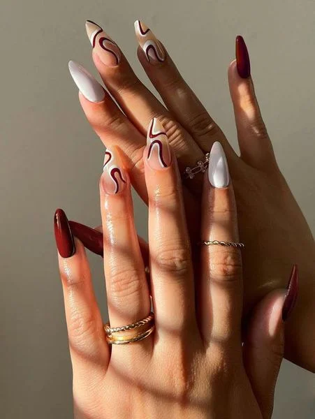 Móng tay dài dáng nhọn với họa tiết trừu tượng đỏ trắng và nude