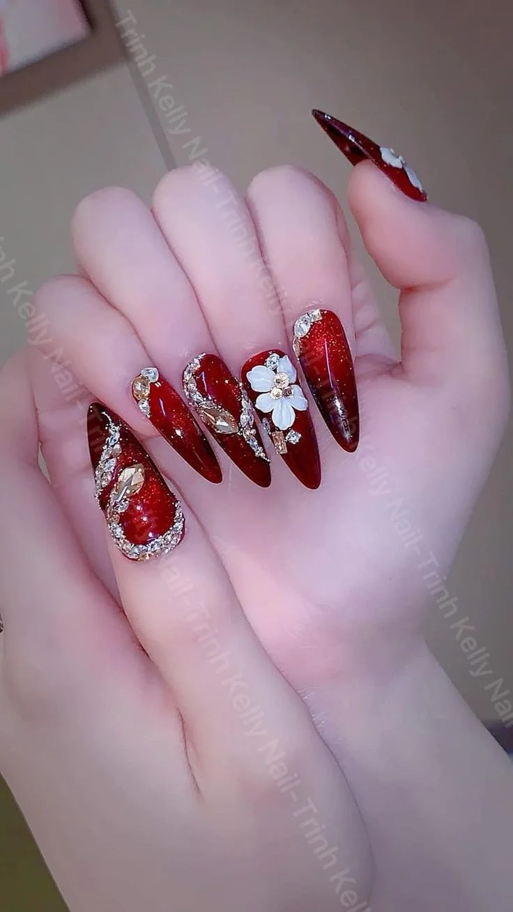 Móng tay dài màu đỏ đính đá và hoa trắng trên nền tím nhạt