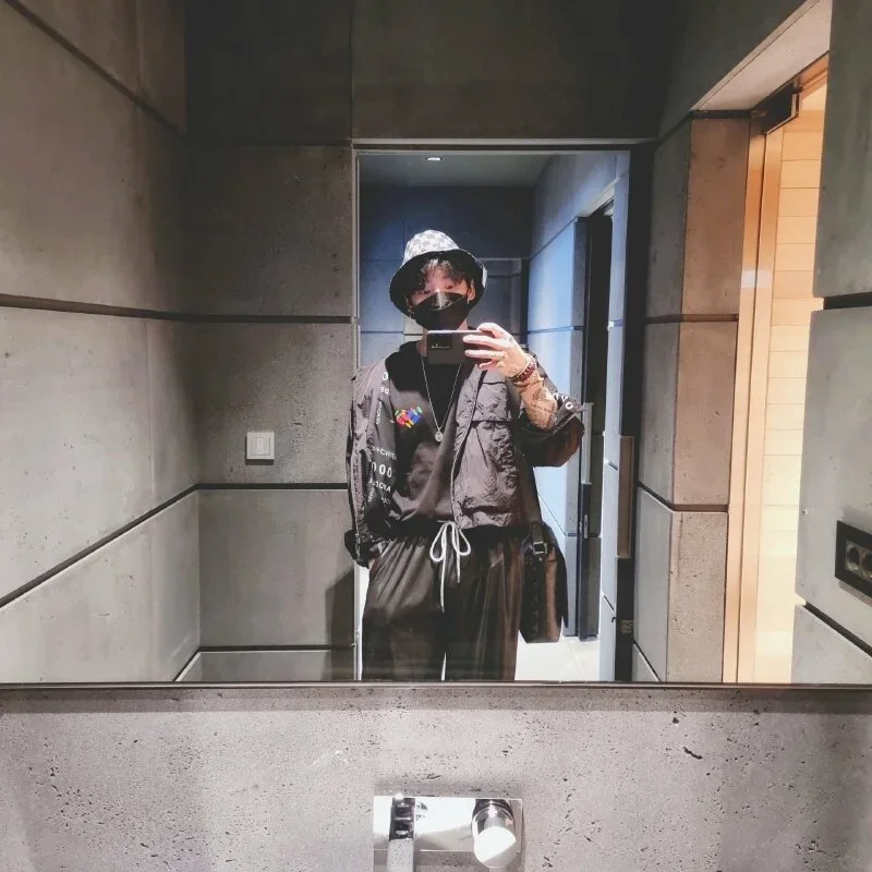 Kiểu selfie nam với bộ quần áo đen cùng chiếc khẩu trang đen, đầu đội nón vành đen cùng những phụ kiện thời trang cá tính, dáng đứng thẳng tự nhiên, một tay bỏ